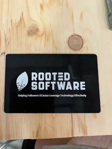 Black metal Rooted Software business card on a wood bench